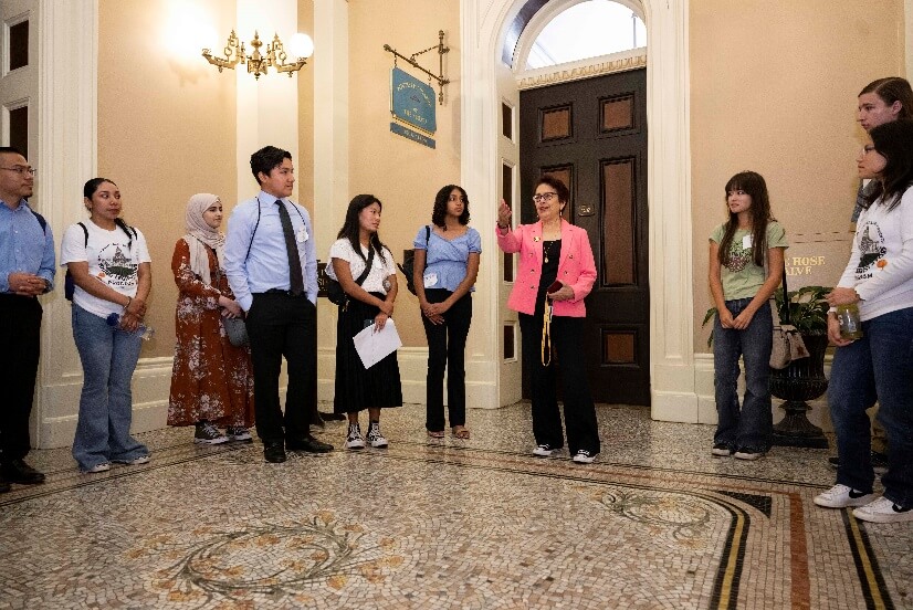 Senator Caballero stands in the Capitol, speaking to a group of high school students. 